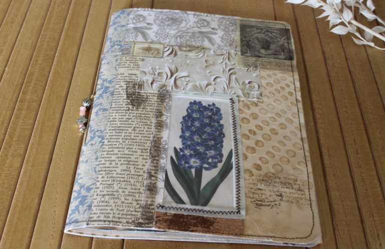 Junk journal Junk journal fermé, couverture en collage de papiers anciens avec une jacinthe bleue, sur un plateau en bois